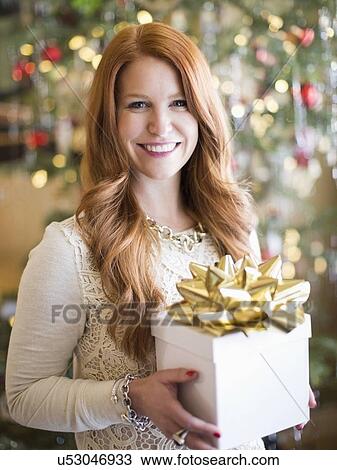 Stock Image - Studio shot of mid adult woman holding present in Christmas time. Fotosearch