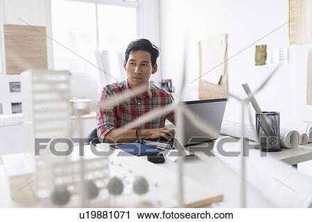 Stock Image - Wind turbine models on desk in front of architect. Fotosearch