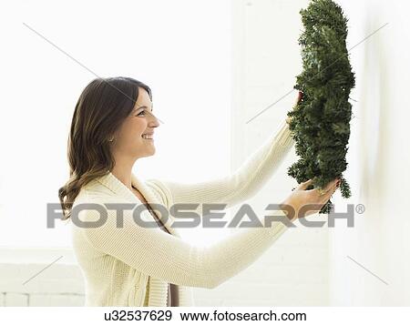 Stock Photo - Woman decorating home with Christmas wreath. Fotosearch