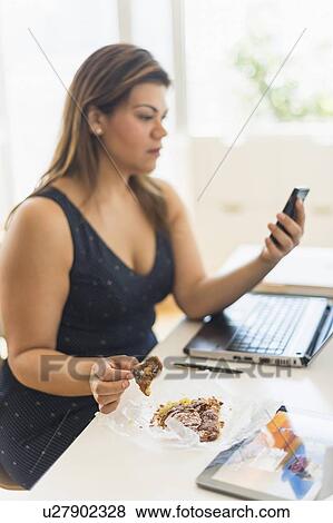Woman eating croissant and using mobile phone in office View Large Photo Image Stock Photo - Woman eating croissant and using mobile phone in office. Fotosearch