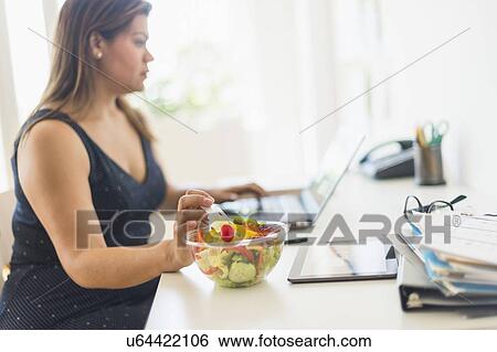 Woman eating salad and using laptop in office View Large Photo Image Stock Photograph - Woman eating salad and using laptop in office. Fotosearch