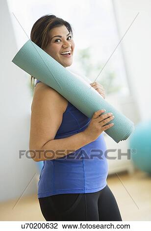 Stock Image - Woman holding exercise mat at gym. Fotosearch
