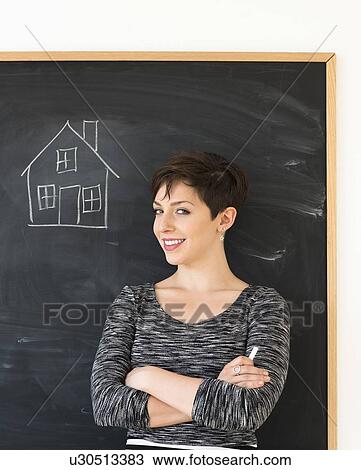 Stock Image - Woman in front of blackboard with house drawing. Fotosearch