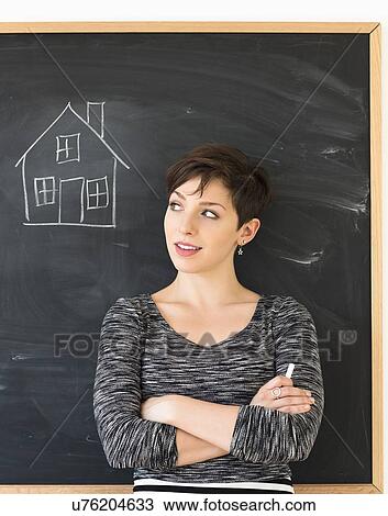 Stock Image - Woman in front of blackboard with house drawing. Fotosearch