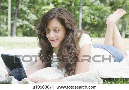 Stock Image - Woman lying on blanket using digital tablet. Fotosearch