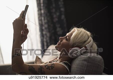 Picture - Woman lying on sofa using digital tablet. Fotosearch