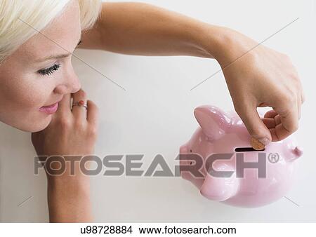 Picture - Woman putting coin into piggy bank. Fotosearch