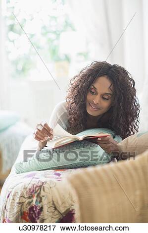 Stock Photo - Woman reading book on bed. Fotosearch