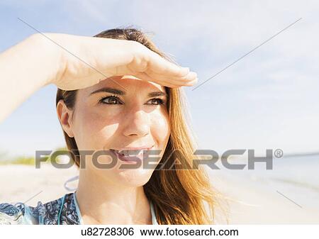 Stock Photograph - Woman shielding eyes on beach. Fotosearch
