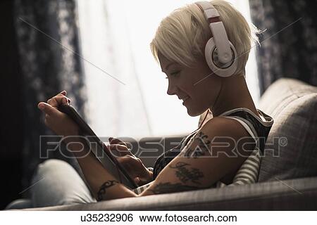 Stock Photograph - Woman sitting on sofa using digital tablet. Fotosearch