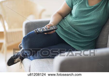 Picture - Woman sitting on sofa with remote control. Fotosearch