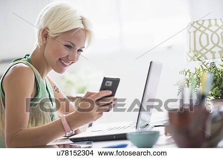 Woman using cell phone and laptop at home View Large Photo Image Picture - Woman using cell phone and laptop at home. Fotosearch