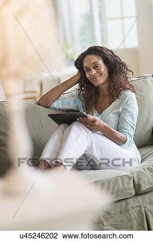 Stock Image - Woman using digital tablet on sofa. Fotosearch