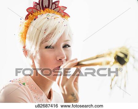 Stock Photograph - Woman wearing tiara blowing party horn blower. Fotosearch