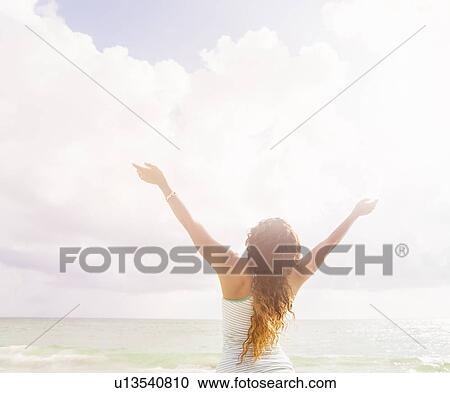 Woman with arms raised standing on beach View Large Photo Image Stock Image - Woman with arms raised standing on beach. Fotosearch
