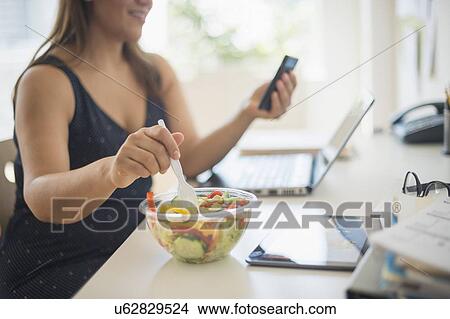 Picture - Woman working in home office and eating salad. Fotosearch
