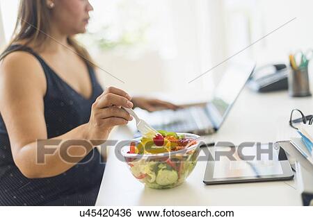 Woman working in home office and eating salad View Large Photo Image Stock Photograph - Woman working in home office and eating salad. Fotosearch