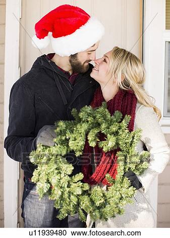 Stock Image - Young couple holding wreath, looking face to face. Fotosearch