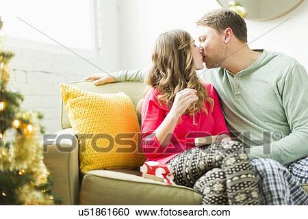 Stock Image - Young couple kissing on sofa at Christmas. Fotosearch