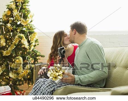 Stock Photograph - Young couple kissing on sofa at Christmas. Fotosearch
