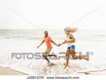 Stock Photo - Young couple running on beach. Fotosearch