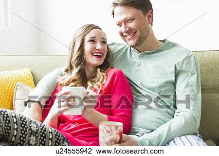 Young couple wearing pajamas sitting on sofa View Large Photo Image Stock Image - Young couple wearing pajamas sitting on sofa. Fotosearch