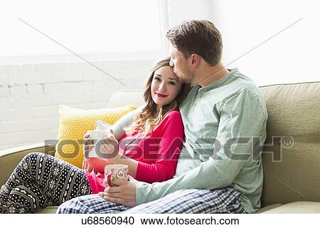 Stock Image - Young couple wearing pajamas sitting on sofa. Fotosearch