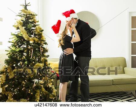 Stock Photo - Young woman and man wearing Santa hats kissing. Fotosearch