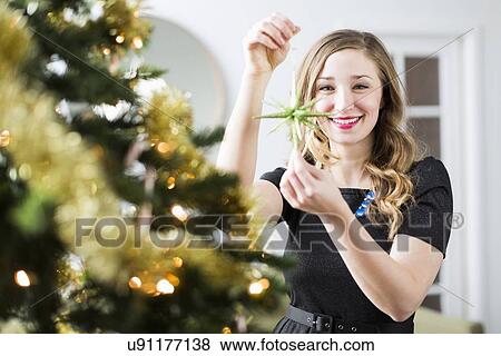 Stock Photo - Young woman decorating Christmas tree. Fotosearch