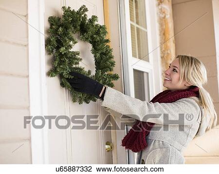 Stock Image - Young woman hanging wreath. Fotosearch