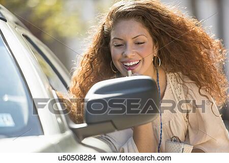 Young woman putting lipstick looking at rear mirror View Large Photo Image Picture - Young woman putting lipstick looking at rear mirror. Fotosearch