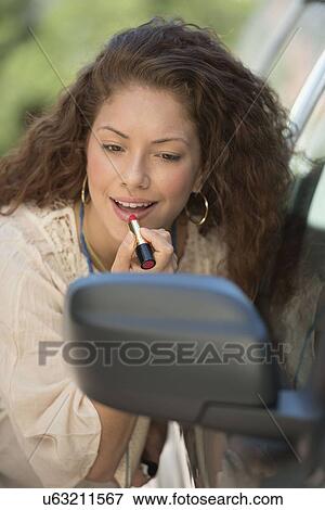 Young woman putting lipstick looking at rear mirror View Large Photo Image Stock Photo - Young woman putting lipstick looking at rear mirror. Fotosearch