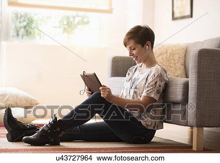 Picture - Young woman sitting on floor and using tablet pc. Fotosearch