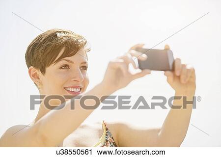 Young woman taking selfie with mobile phone View Large Photo Image Stock Image - Young woman taking selfie with mobile phone. Fotosearch