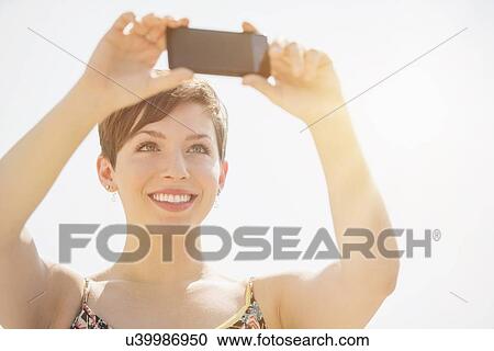 Stock Image - Young woman taking selfie with mobile phone. Fotosearch
