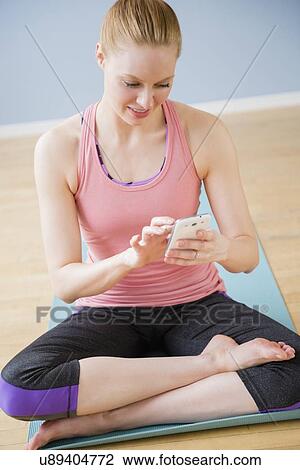 Young woman using mobile phone sitting on exercise mat View Large Photo Image Stock Image - Young woman using mobile phone sitting on exercise mat. Fotosearch