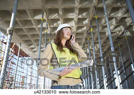 Stock Image - Architect chatting on smartphone on construction site. Fotosearch
