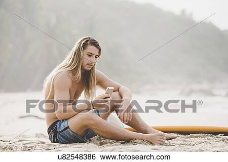 Stock Photograph - Australian surfer using smartphone, Bacocho, Puerto Escondido, Mexico. Fotosearch