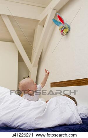Baby girl pointing from bed whilst mother under covers View Large Photo Image Stock Image - Baby girl pointing from bed whilst mother under covers. Fotosearch
