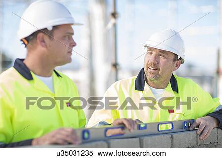 Stock Photography - Builder and site manager using spirit level on construction site wall. Fotosearch