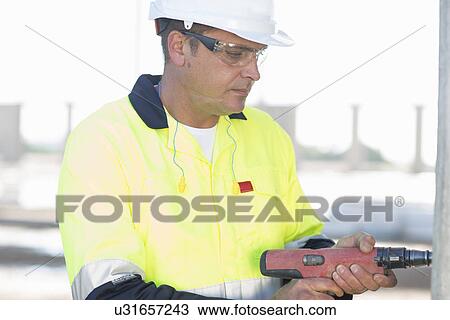 Stock Image - Builder using electric drill on construction site. Fotosearch