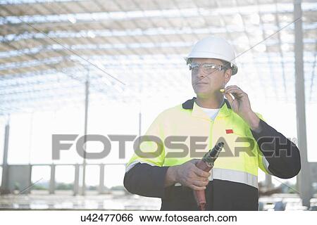 Stock Photograph - Builder with electric drill inserting earplugs on construction site. Fotosearch