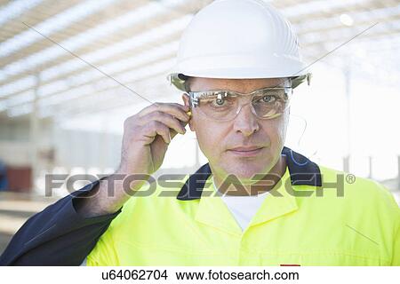 Picture - Builder with safety glasses inserting earplugs on construction site. Fotosearch