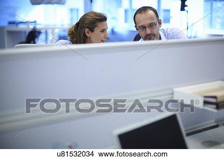 Picture - Businessman and businesswoman chatting at their desks in office. Fotosearch