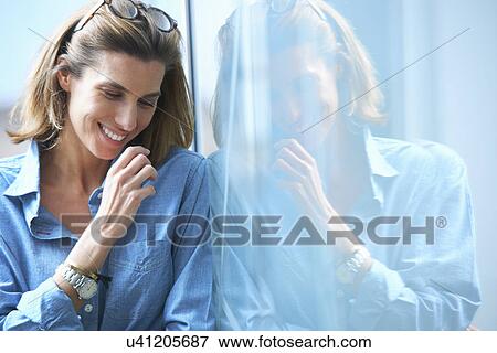 Candid shot of mid adult businesswoman leaning against glass wall in office View Large Photo Image Stock Photo - Candid shot of mid adult businesswoman leaning against glass wall in office. Fotosearch
