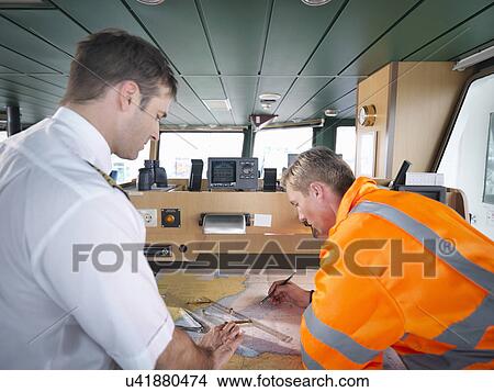 Picture - Captain and navigator checking charts on ship's bridge, rear view. Fotosearch