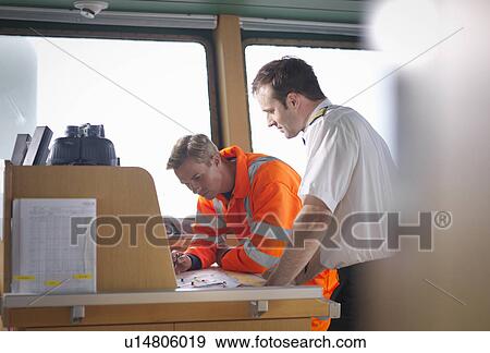 Stock Photo - Captain and navigator checking charts on ship's bridge. Fotosearch