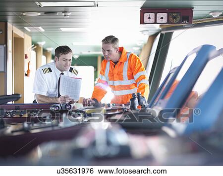 Captain and worker discussing notes on ship's bridge View Large Photo Image Stock Photograph - Captain and worker discussing notes on ship's bridge. Fotosearch