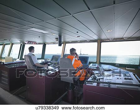 Captain and worker on bridge steering ship at sea View Large Photo Image Stock Photo - Captain and worker on bridge steering ship at sea. Fotosearch