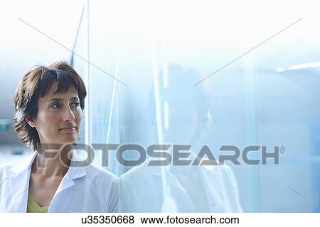 Stock Photo - Confident mature businesswoman leaning against glass wall in office. Fotosearch
